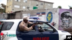 A Haitian national police officer fires birdshot at demonstrators during a street protest after it was announced that the Jan. 24 runoff election had been postponed, in Port-au-Prince, Jan. 22, 2016.