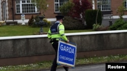 FILE - An Irish police officer removes a Garda checkpoint sign at the Armagh and County Louth border between Northern Ireland and Ireland, during a visit by European Union Chief Negotiator for Brexit Michel Barnier, May 12, 2017. 