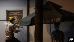 A worker tries to remove the plaque from the United States Consulate near a Chinese paramilitary policeman on guard in Chengdu in southwest China's Sichuan province on Sunday, July 26, 2020. The ongoing sharp deterioration in U.S.-China ties poses risks t