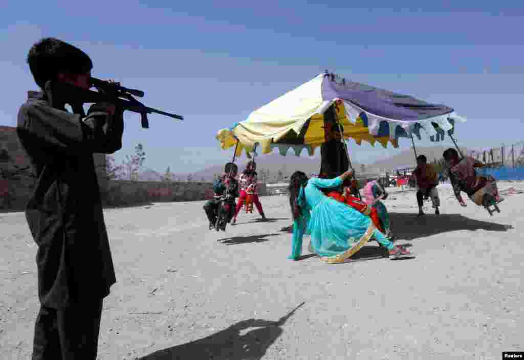 아프가니스탄 카불에서 이드 알피트르 축제가 시작된 가운데, 한 소년이 장남감총에 달린 조준경을 통해 놀이터의 어린이들을 보고 있다.