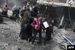 A Syrian woman and children run for cover amid the rubble of buildings following government bombing in the rebel-held town of Hamouria, in the besieged Eastern Ghouta region on the outskirts of Damascus, Feb. 19, 2018.
