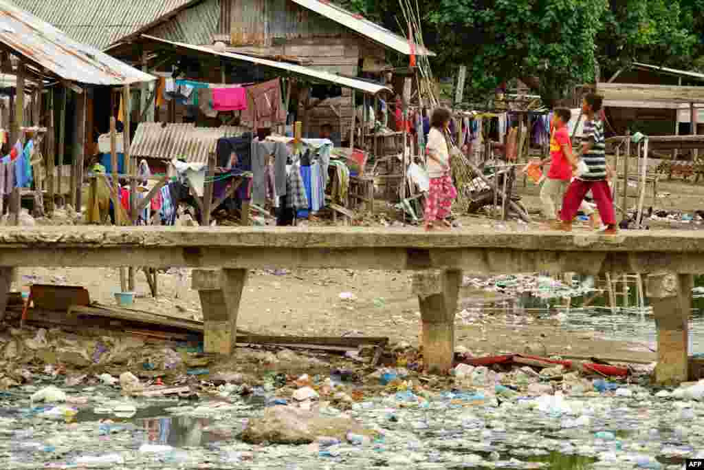 Residents cross a bridge at a river mouth filled with garbages in Lhokseumawe, Aceh, Indonesia.