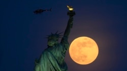 A helicopter flies past as the full moon rises behind the Statue of Liberty on May 18, 2019 in New York City.