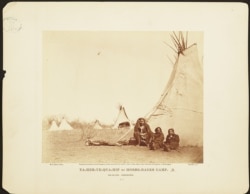Circa 1873 photograph shows three Comanche Indian men in front of teepee in encampment at Fort Sill, Indian Territory (present-day Oklahoma).