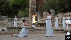 Actress Katerina Lehou, right, as high priestess, lights the torch during the lighting ceremony of the Olympic flame in Ancient Olympia, southwestern Greece, Oct. 24, 2017. 