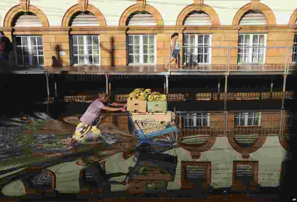 A man pushing a shopping cart loaded with bananas wade through a flooded street in downtown Manaus, Amazonas state, Brazil.