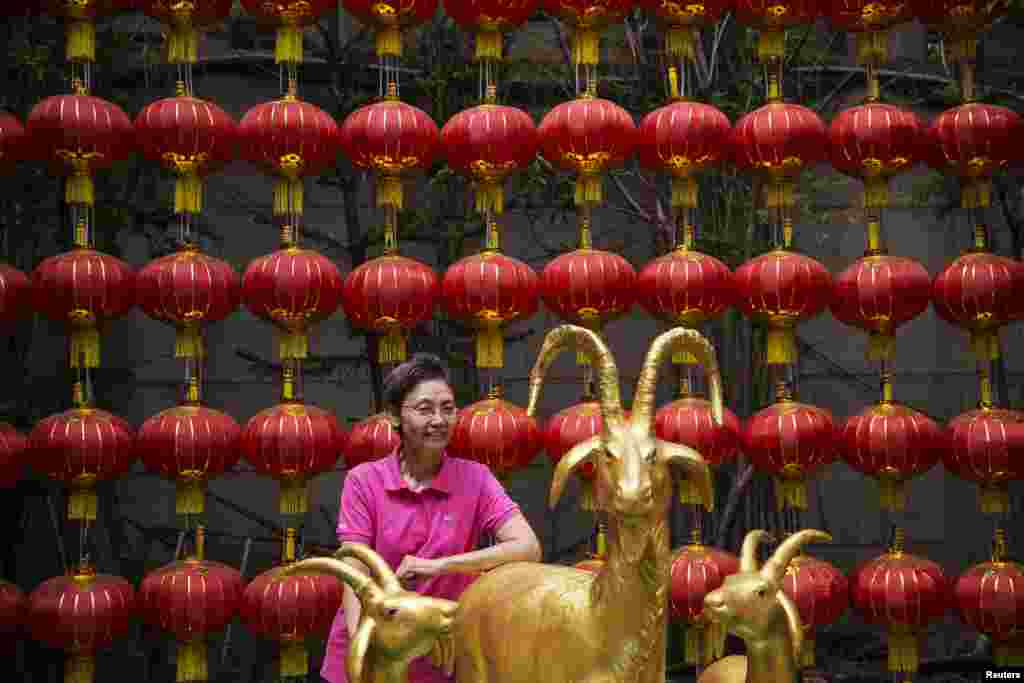 A woman stands behind statues of goats at a temple decorated for the Chinese Lunar New Year in Chinatown, Bangkok, Thailand, Feb. 19, 2015.