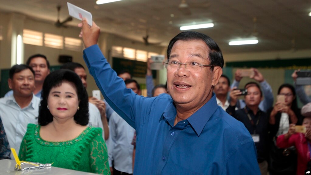 Cambodian Prime Minister Hun Sen of the Cambodian People's Party shows off his ballot paper next to his wife, Bun Rany, foreground left, before voting in local elections at Takhmau polling station in Kandal province, southeast of Phnom Penh, Cambodia, Sunday, June 4, 2017. (AP Photo/Heng Sinith)