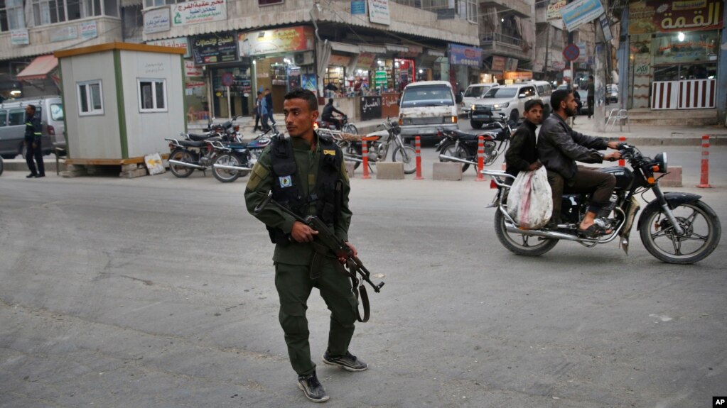 FILE - A member of the Kurdish internal security forces patrols a commercial street in Manbij, northern Syria, March 28, 2018. Manbij, a mixed Arab and Kurdish town of nearly 400,000, was freed from Islamic State militants in 2016 by YPG fighters with the backing of U.S. forces.