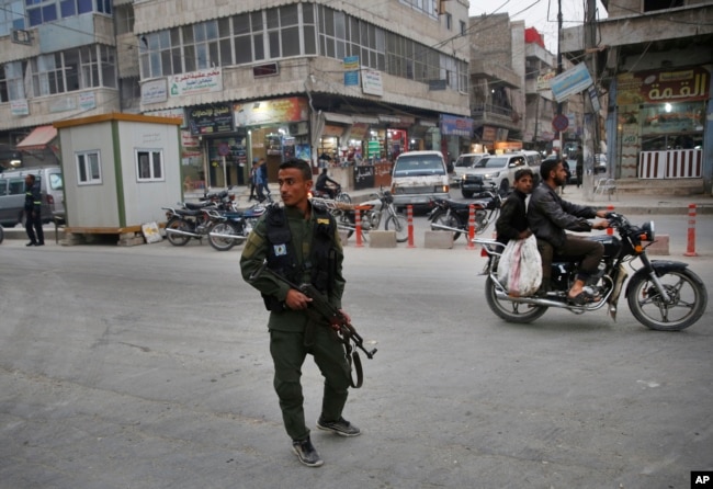 FILE - A member of the Kurdish internal security forces patrols a commercial street in Manbij, north Syria, March 28, 2018. Manbij, a mixed Arab and Kurdish town of nearly 400,000, was liberated from Islamic State militants in 2016 by the YPG fighters with backing from U.S-led coalition airstrikes.