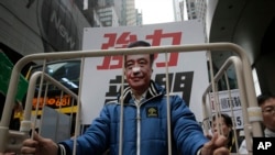 FILE - A protester wearing a mask of missing bookseller Lee Bo sits in a cage during a protest against the disappearances of booksellers in Hong Kong. The case has raised fears about Beijing eroding civil liberties in Hong Kong.