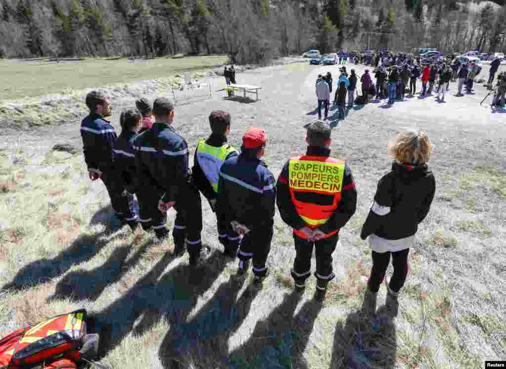 Rescuers stand nearby while relatives pay their respects at the memorial for the victims of the air disaster in the village of Le Vernet, in the French Alps, March 27, 2015.