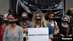 Wearing a gag over her mouth, a woman holds a sign that reads in Portuguese "Down the dictatorship" during an act organized by the NGO Rio de Paz to remember the victims of Brazil's dictatorship, in Rio de Janeiro, Brazil, Dec. 8, 2018. 