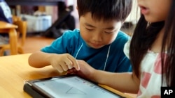 FILE - Children work on a digital program at Coby Preschool in Yoshikawa, suburban Tokyo, on an assignment, which was to draw on a triangle on an iPad, July 12, 2018.