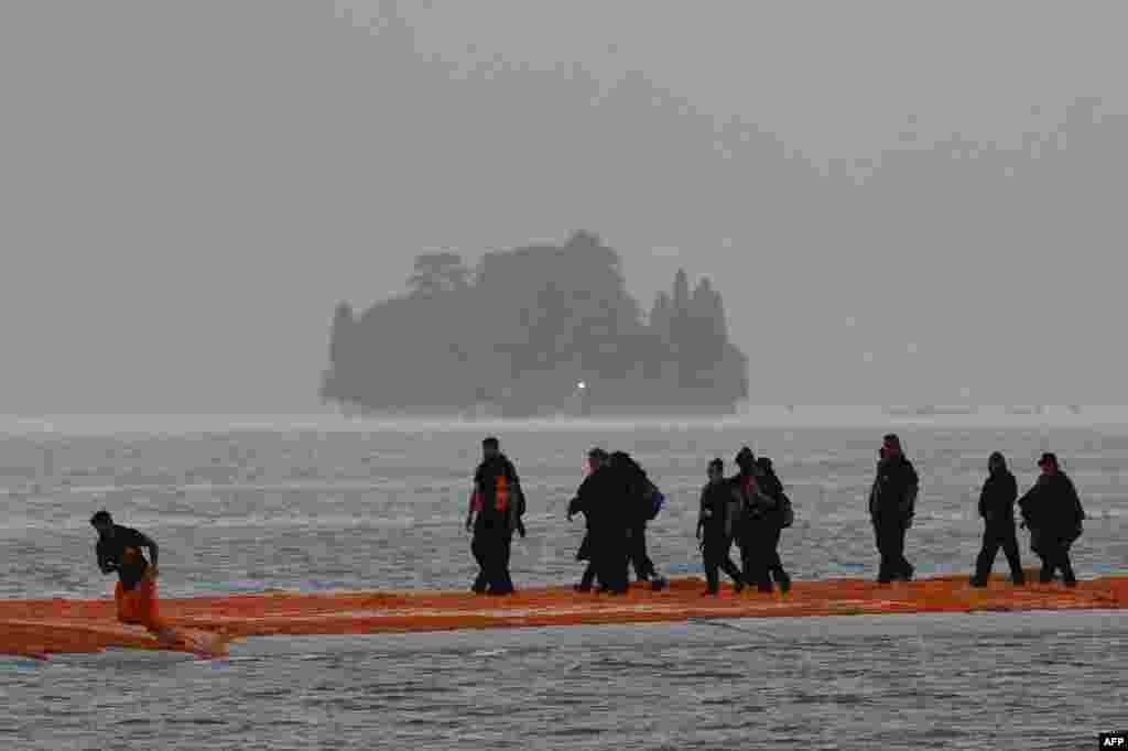 People work under heavy rain on the monumental installation &quot;The Floating Piers&quot; created by artists Christo and Jeanne-Claude on the lake Iseo, northern Italy. Some 200,000 floating cubes create a 3-kilometers runway connecting the village of Sulzano to the small island of Monte Isola on the Iseo Lake for a 16-day outdoor installation opening on June 18.