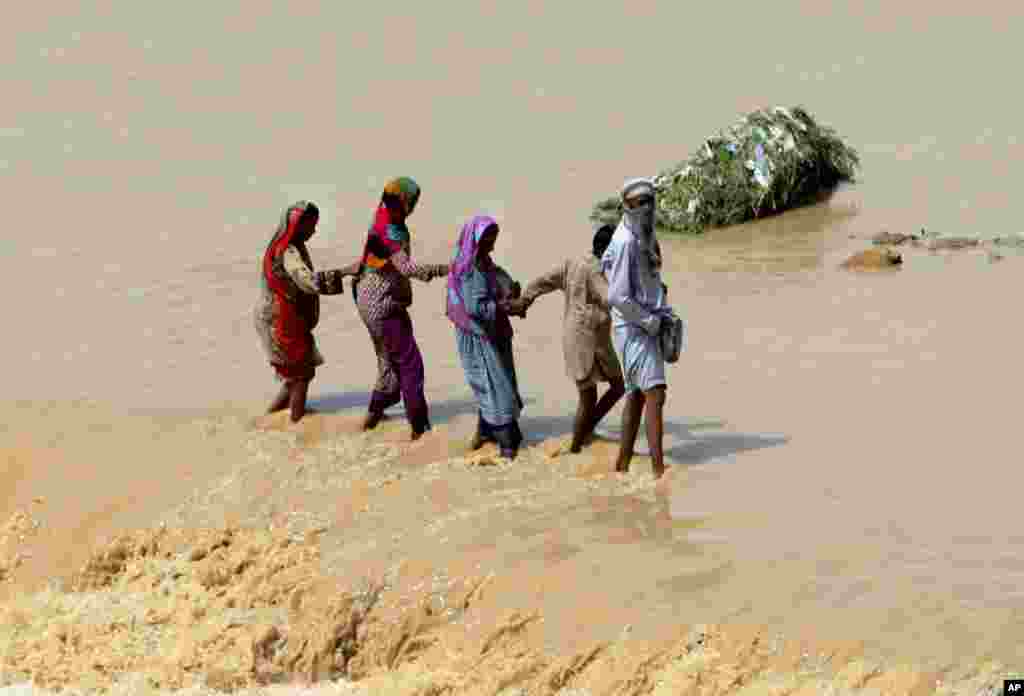 Pakistani family members help each others to cross stream caused by heavy rainfall in Karachi.