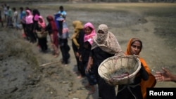 FILE - Rohingya refugee women carry baskets of dried out mud from the riverbed to help raise the ground level of their camp in preparation for monsoon season, in Shamlapur refugee camp, in Cox's Bazaar, Bangladesh, March 24, 2018.