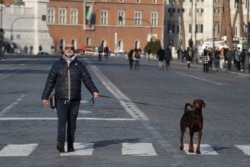 FILE - A man enjoys a stroll with his dog on the empty Via Dei Fori Imperiali avenue during a no traffic day, in Rome, Jan. 19, 2020.
