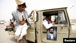 An image of al-Houthi Hussein Badr Eddin al-Huthi, the late founder of Yemen's al-Houthi Shi'ite group, is seen on a vehicle as his follower jumps from it while carrying a weapon to secure a road in the northwestern province of Saada, June 4, 2013.