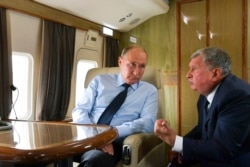 FILE - Russian President Vladimir Putin, left, listens to Russian Rosneft CEO Igor Sechin during his flight to visit Chernigovets coal mine, in Beryozovsky, Kemerovo region, Russia, Monday, Aug. 27, 2018.