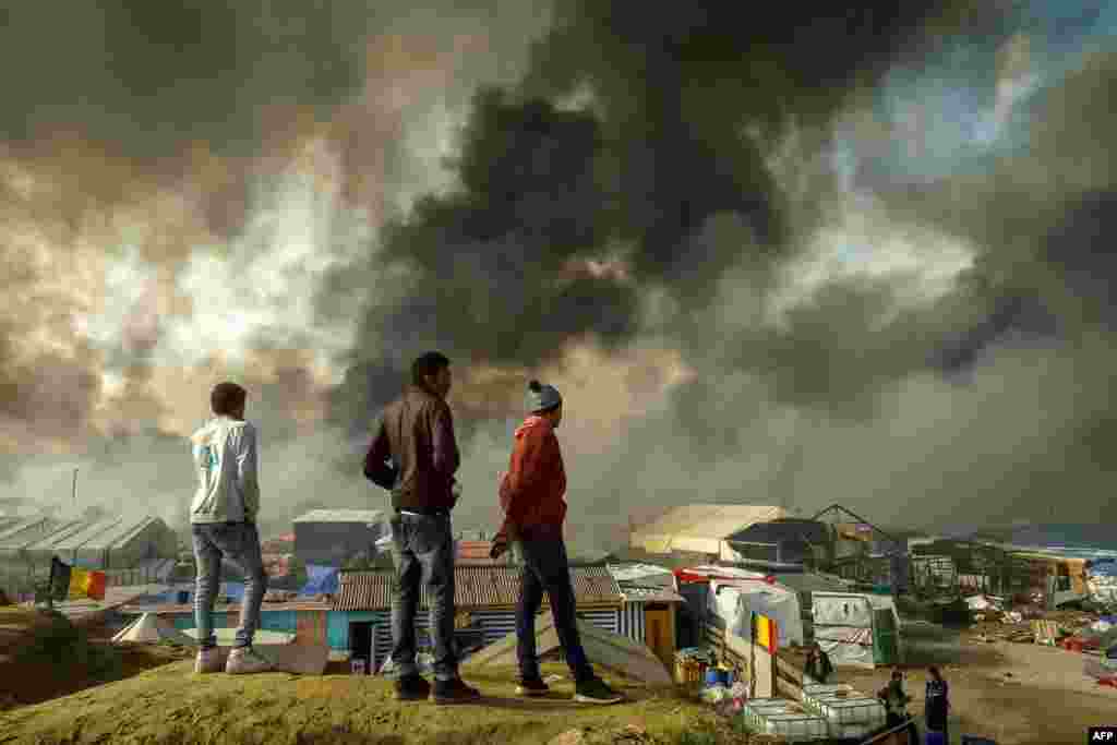 Migrants stand on a hill overlooking the &quot;Jungle&quot; migrant camp in Calais, northern France, as smoke rises during a massive operation to clear the squalid settlement where 6,000-8,000 people have been living in dire conditions.