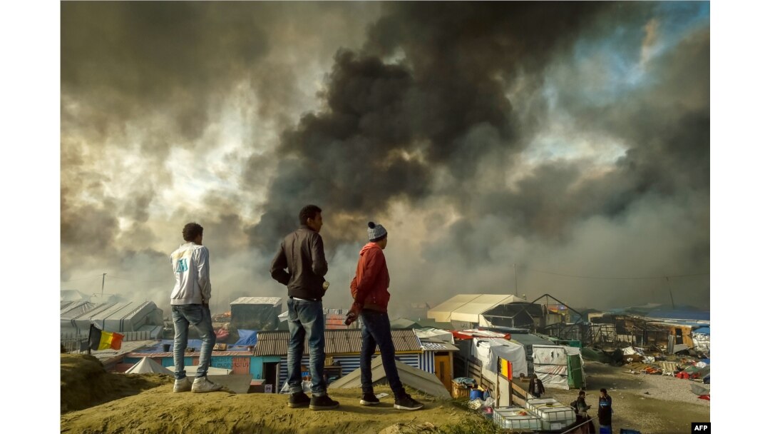 Migrants stand on a hill overlooking the "Jungle" migrant camp in Calais, northern France, as smoke rises, Oct. 26, 2016, during a massive operation to clear the squalid settlement where 6,000-8,000 people have been living in dire conditions.