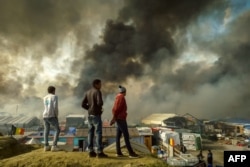 Migrants stand on a hill overlooking the "Jungle" migrant camp in Calais, northern France, as smoke rises, Oct. 26, 2016, during a massive operation to clear the squalid settlement where 6,000-8,000 people have been living in dire conditions.