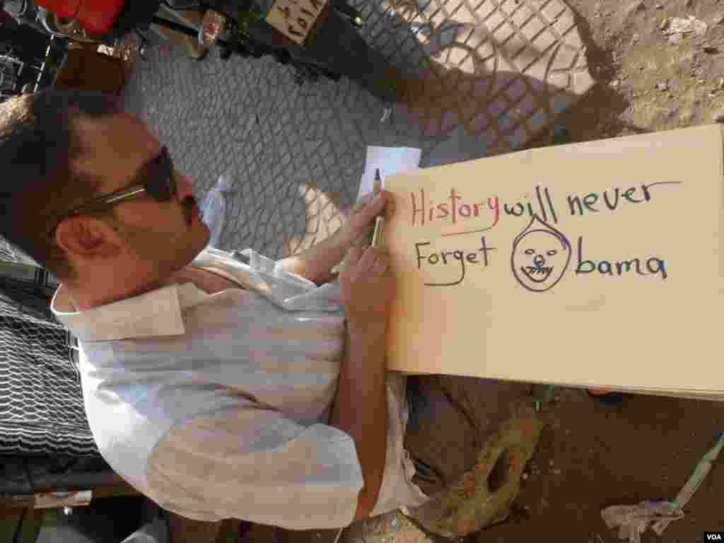 A man in Tahrir Square writes on a poster &quot;History Will Never Forget Obama,&quot; July 7, 2013 (S. Behn/VOA)