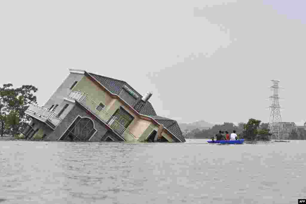 Residents ride a boat past a damaged house near the Poyang Lake due to torrential rains in Poyang county, Shangrao city in China&#39;s central Jiangxi province, July 15, 2020.