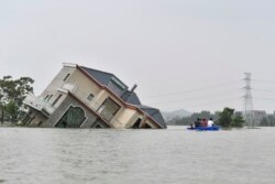 This photo taken on July 15, 2020 shows residents riding a boat past a damaged and flood-affected house near the Poyang Lake due to torrential rains in Poyang county, Shangrao city in China's central Jiangxi province.