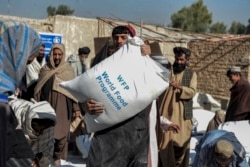 Warga Afghanistan membawa karung-karung berisi makanan yang dibagikan sebagai bantuan Program Pangan Dunia (WFP) di Kandahar pada 19 Oktober 2021. (Foto: AFP/Javed Tanveer)