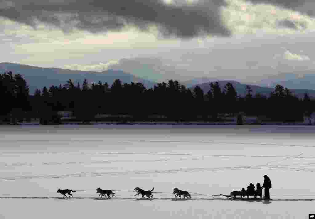 Sekawanan anjing menarik kereta luncur dengan penumpangnya di wilayah dengan latar belakang pemandangan yang indah di sekitar Danau Mirror di Lake Placid, New York. 