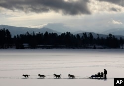 FILE - A dogsled team pulls passengers on a scenic ride across Mirror Lake, Jan. 17, 2014, in Lake Placid, New York. (AP Photo/Mike Groll)