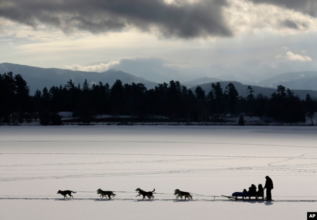 FILE - A dogsled team pulls passengers on a scenic ride across Mirror Lake, Jan. 17, 2014, in Lake Placid, New York. (AP Photo/Mike Groll)