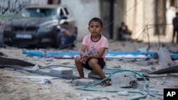 A Palestinian boy sits looking at others inspecting the damage of their shops following Israeli airstrikes on Jabaliya refugee camp, northern Gaza Strip.