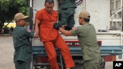 Yem Chroeum, center, an unlicensed medical practitioner, is assisted by prison guards to get off a truck upon his arrival at the Battambang provincial court in Battambang province, northwest of Phnom Penh, Cambodia, Thursday, Dec. 3, 2015. The Cambodian c