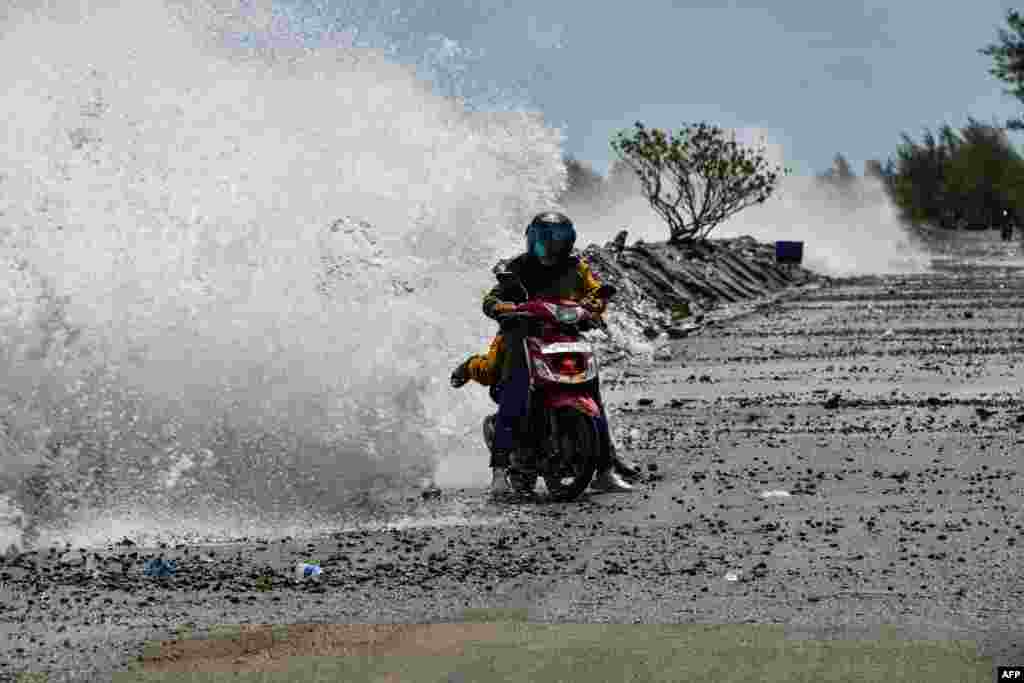 People on motorbikes are hit by large waves breaking on the shores of Banda Aceh, Indonesia.
