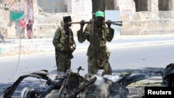 Somali government soldiers look at the wreckage of a mangled car used by a suicide bomber at the scene of a bomb attack next to a tea shop in the suburbs of capital Mogadishu February 27, 2014.