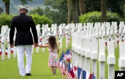 FILE - A U.S. Marine Corps soldier holds hands with a small girl as they walk among headstones of World War I dead at a Memorial Day commemoration at the Aisne-Marne American Cemetery in Belleau, France, May 27, 2018.