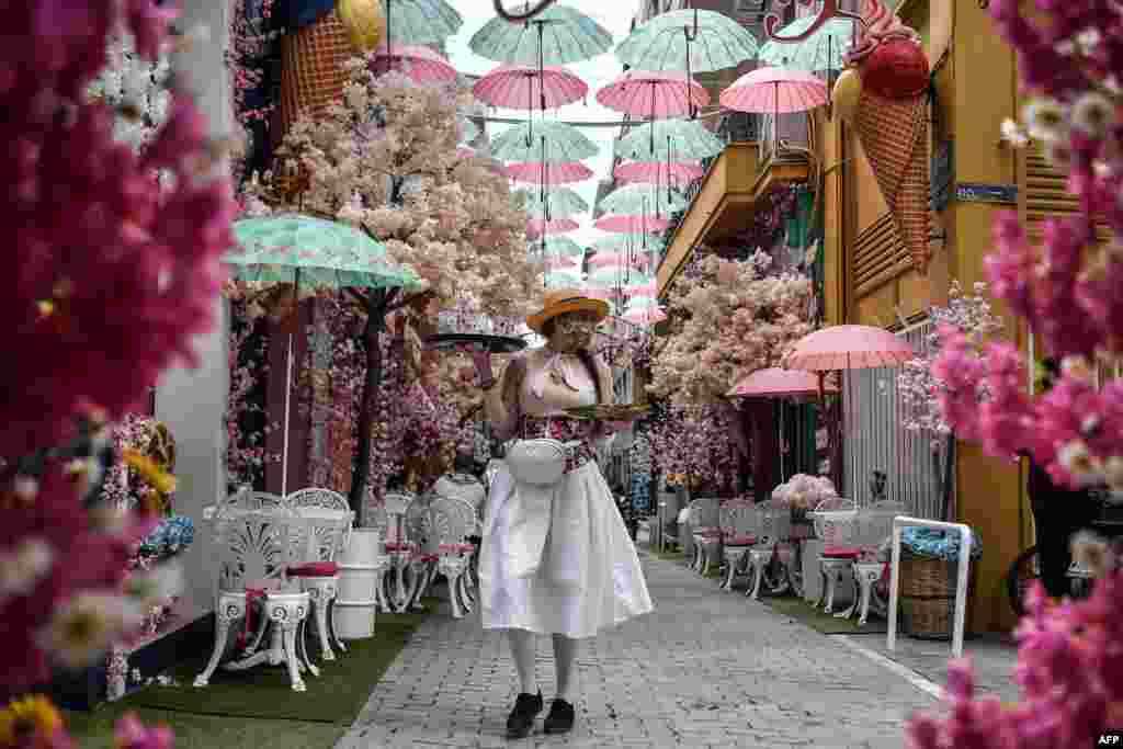 A waitress wearing a homemade protective floral mask and pink gloves serves clients at a thematic outdoor cafe in Athens, as cafes, bars and restaurants reopen after the coronavirus lockdown.