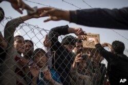 FILE - Displaced Iraqis gather by the fence to buy food and supplies from vendors standing outside the newly opened Chamakor camp, east of Mosul, Iraq, March 12, 2017.