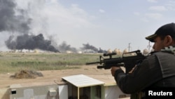 26일 이라크 정부군 병사가 바그다그 북부에서 경계근무를 서고 있다. 정유시설에서 연기가 치솟는 것이 보인다.