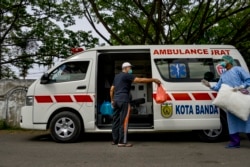 Seorang pasien virus corona (kiri) berbincang dengan petugas medis sebelum naik ke ambulans untuk pulang ke rumahnya dari RSUD Zainoel Abidin di Banda Aceh, 13 April 2020. (Foto: AFP)