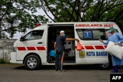 Seorang pasien virus corona (kiri) berbincang dengan petugas medis sebelum naik ke ambulans untuk pulang ke rumahnya dari RSUD Zainoel Abidin di Banda Aceh, 13 April 2020. (Foto: AFP)