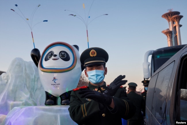 Petugas polisi paramiliter memberi isyarat kepada fotografer di depan maskot Olimpiade Musim Dingin Beijing 2022 di Beijing, China, 15 Januari 2022. (Foto: REUTERS/Thomas Peter)