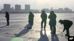 In this Jan. 18, 2016 image made from video, North Koreans stand on the frozen Taedong River as a man, right, ice fishes in Pyongyang, North Korea. 