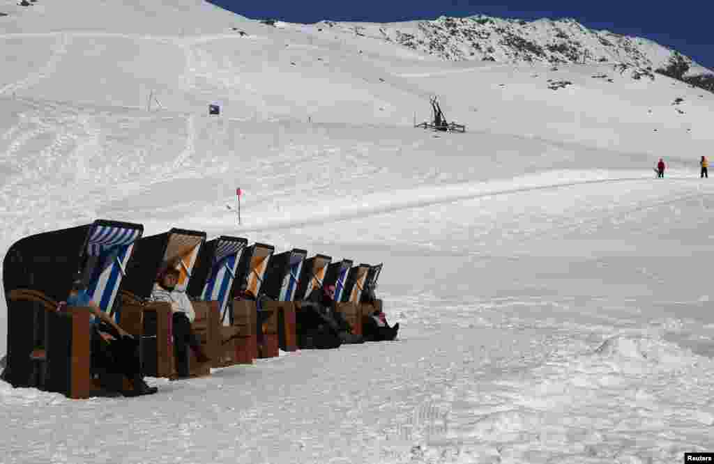 People sit in beach chairs and enjoy sunny winter weather on the Muottas Muragle mountain, at 2546 meters (8058 feet) of altitude near the mountain resort of St. Moritz, Switzerland.