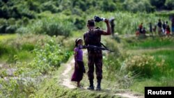 FILE - A member of Border Guard Bangladesh (BGB) tells a Rohingya girl not to come on Bangladesh side, in Cox’s Bazar, Bangladesh.