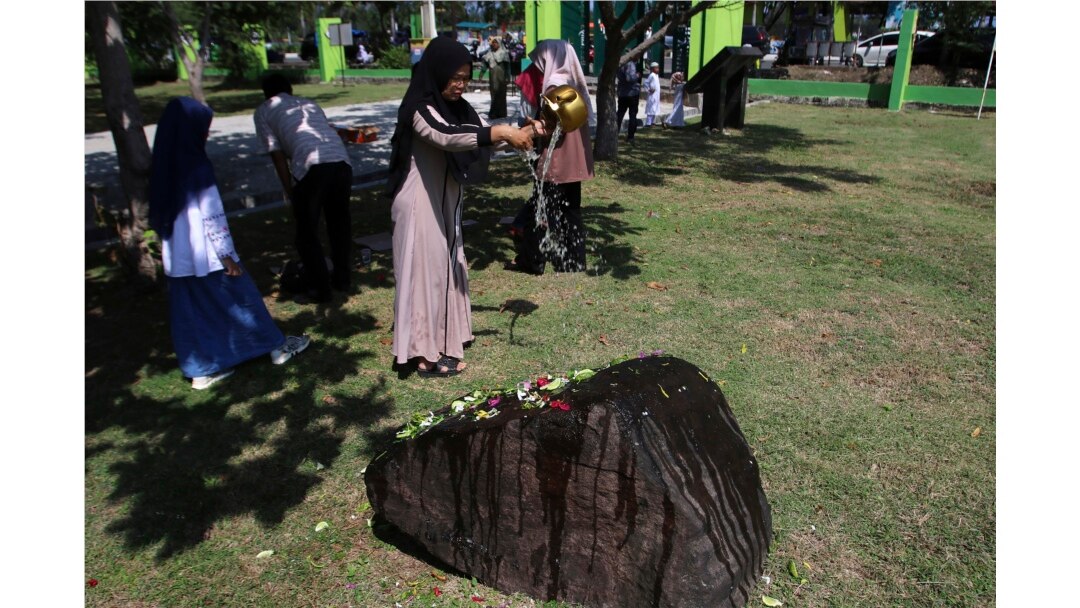 Seorang warga menuangkan air ke sebuah batu yang menandai kuburan massal bagi para korban tsunami Samudra Hindia dalam peringatan 15 tahun bencana di Banda Aceh, Kamis, 26 Desember 2019. (Foto AP / Nurhasanah)