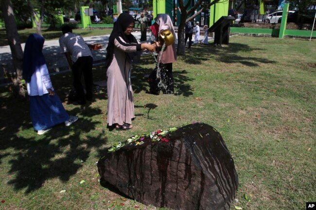 Seorang warga menuangkan air ke sebuah batu yang menandai kuburan massal bagi para korban tsunami Samudra Hindia dalam peringatan 15 tahun bencana di Banda Aceh, Kamis, 26 Desember 2019. (Foto AP / Nurhasanah)